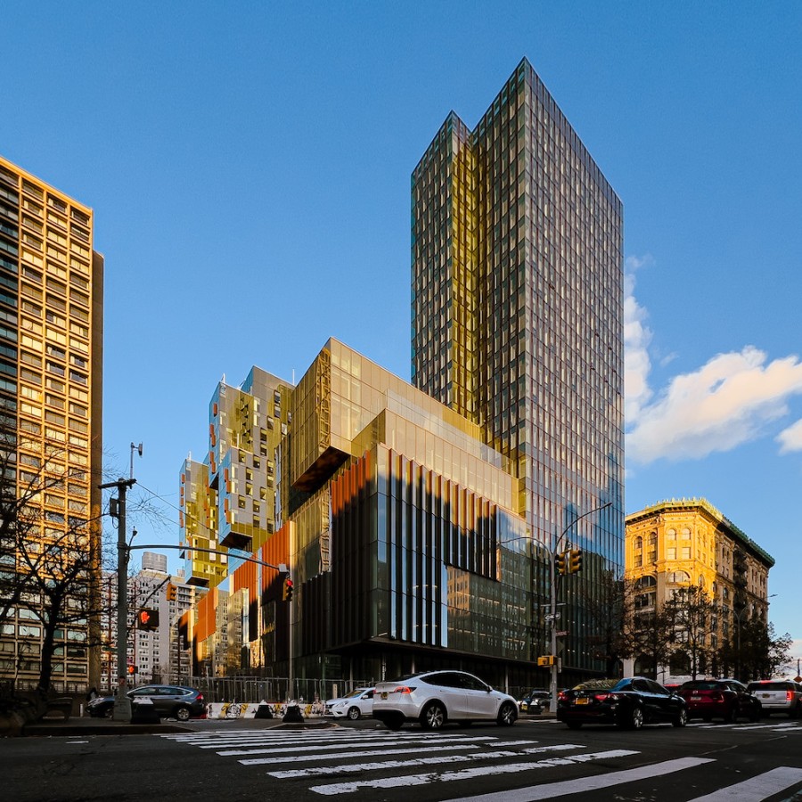 A tall building complex with a glass exterior in daylight with traffic passing in front of the building.