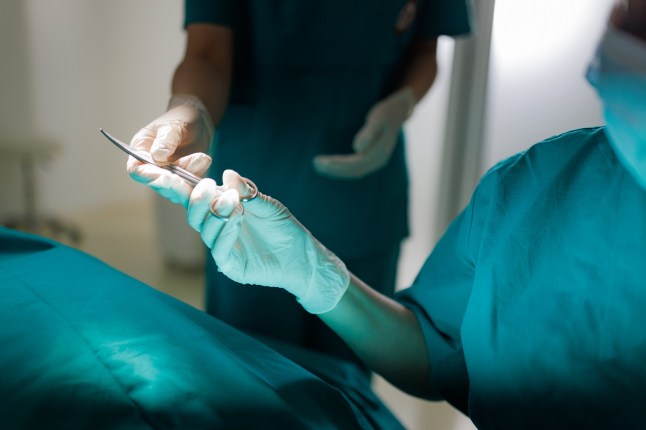 Surgeon carries out surgery on a patient while a nurse provides surgical scissors, illustrating the vital support role that surgical nurses play in complex procedures.